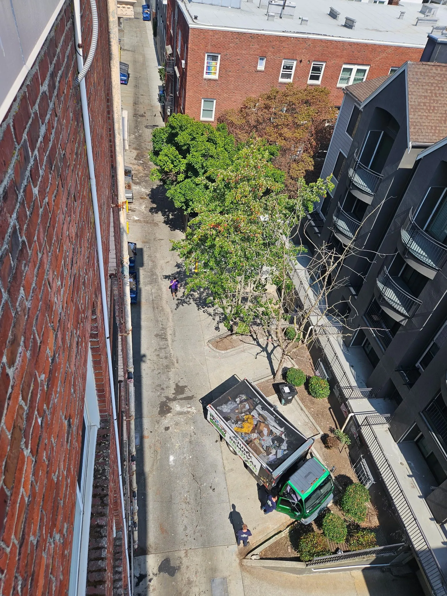 The same alley from the same vantage point, swept clear, with the crew loading the last of it into the truck